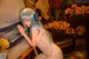 A woman with blue hair and headphones leaning against a painting.
