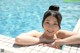 A woman in a white bikini leaning on the edge of a swimming pool.