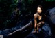 A woman in a black bathing suit sitting on a rock.