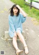 A woman sitting on a concrete bench wearing a blue sweater dress.